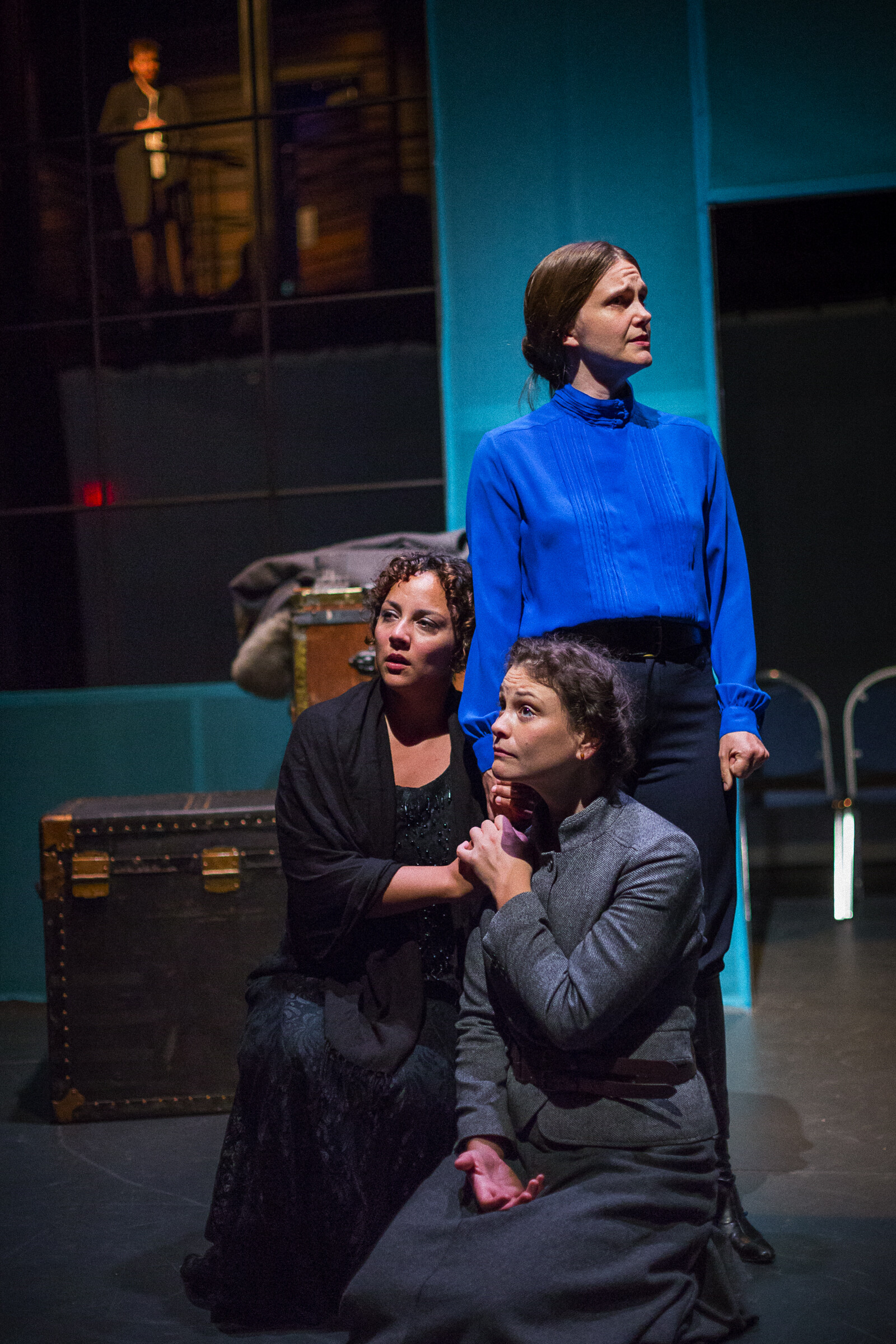 Two women kneeling on the ground and looking concerned, and a third women stands behind them.