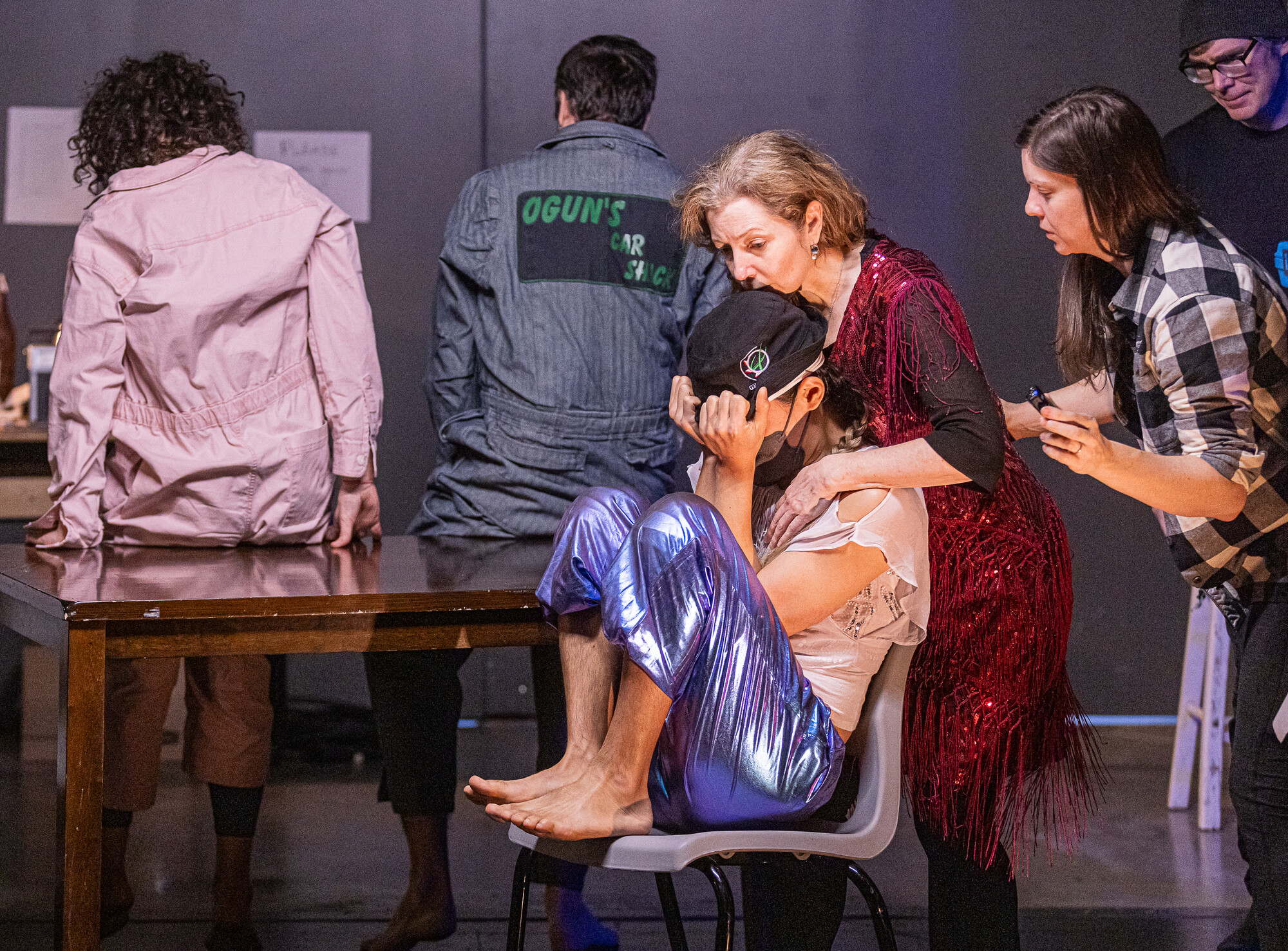 A person in the fetal position in a chair being consoled by others.