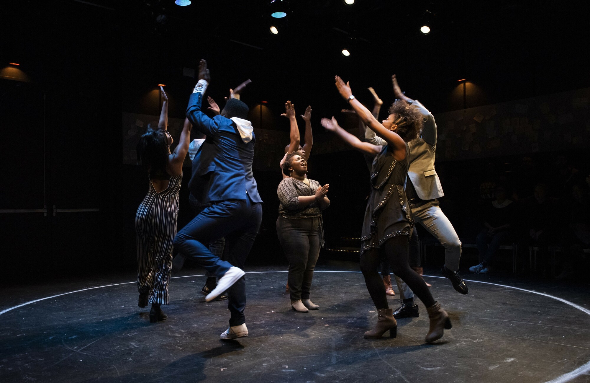 A group of people dancing in a circle and throwing their hands up in the air.