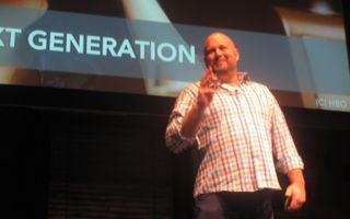 A man on stage with a presentation behind him.