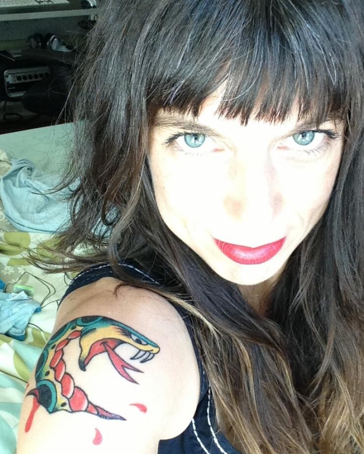 A woman with a tattoo of a snake on her shoulder taking a selfie from a high angle.