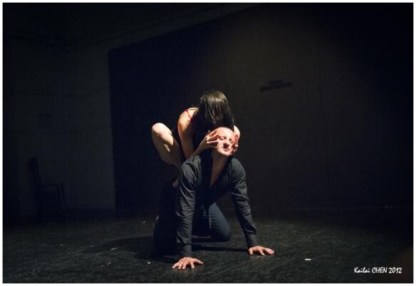 A person crouching on stage with another person behind them grabbing on their face.