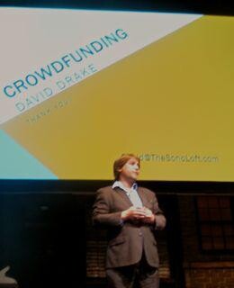 A person in a suit standing on stage in front of a presentation.