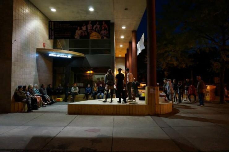 A group of people sitting outside near a building at night.