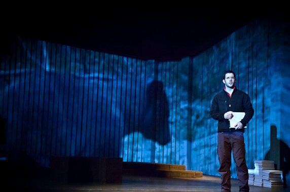 A man on stage with the projection of a bear behind him.