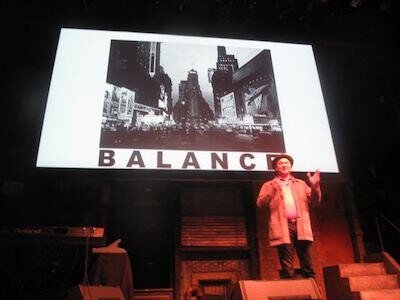 A person on stage with a presentation screen behind them.