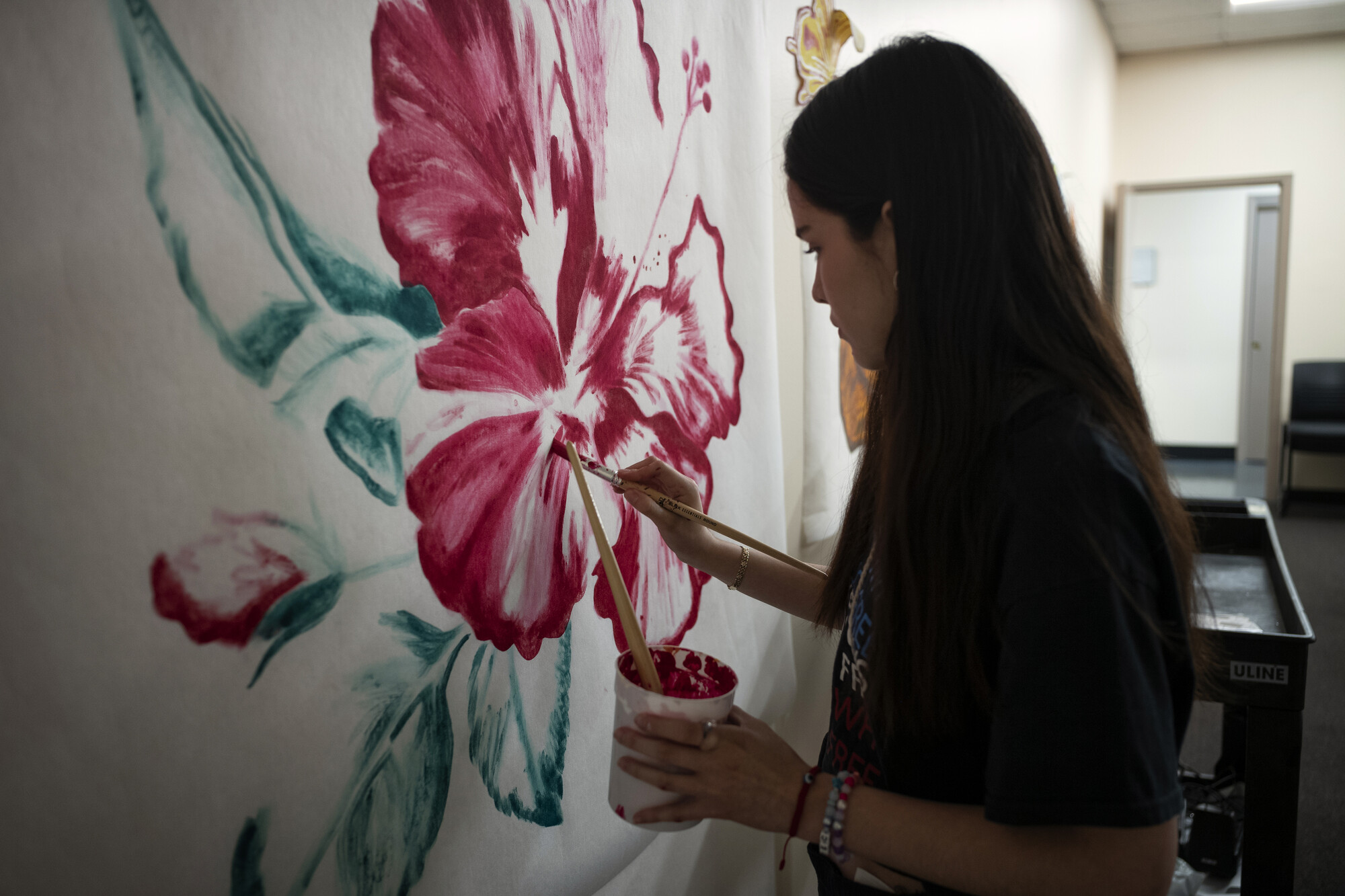 A woman painting a pink hibiscus flower on a wall.