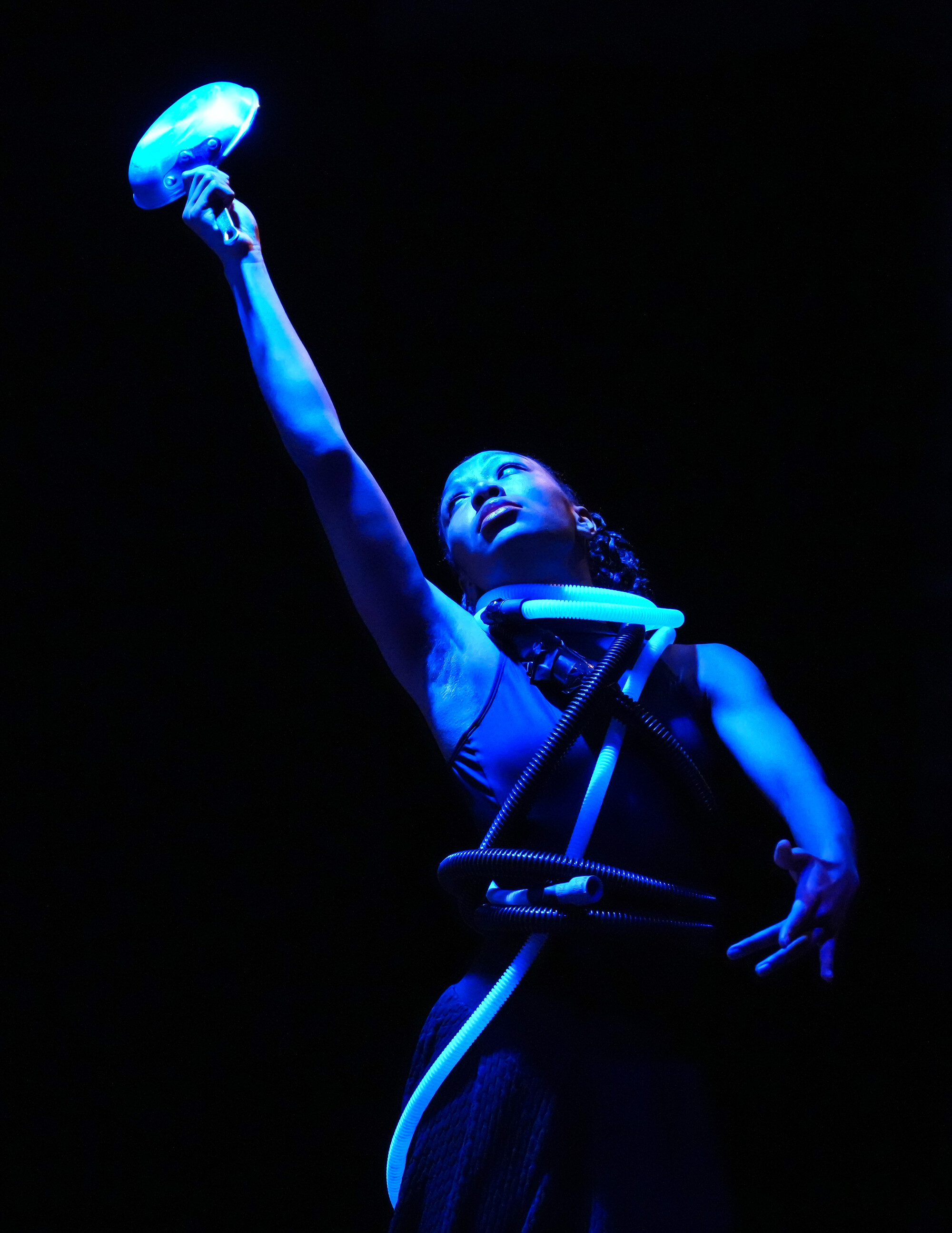 A woman in blue light reaches upwards.