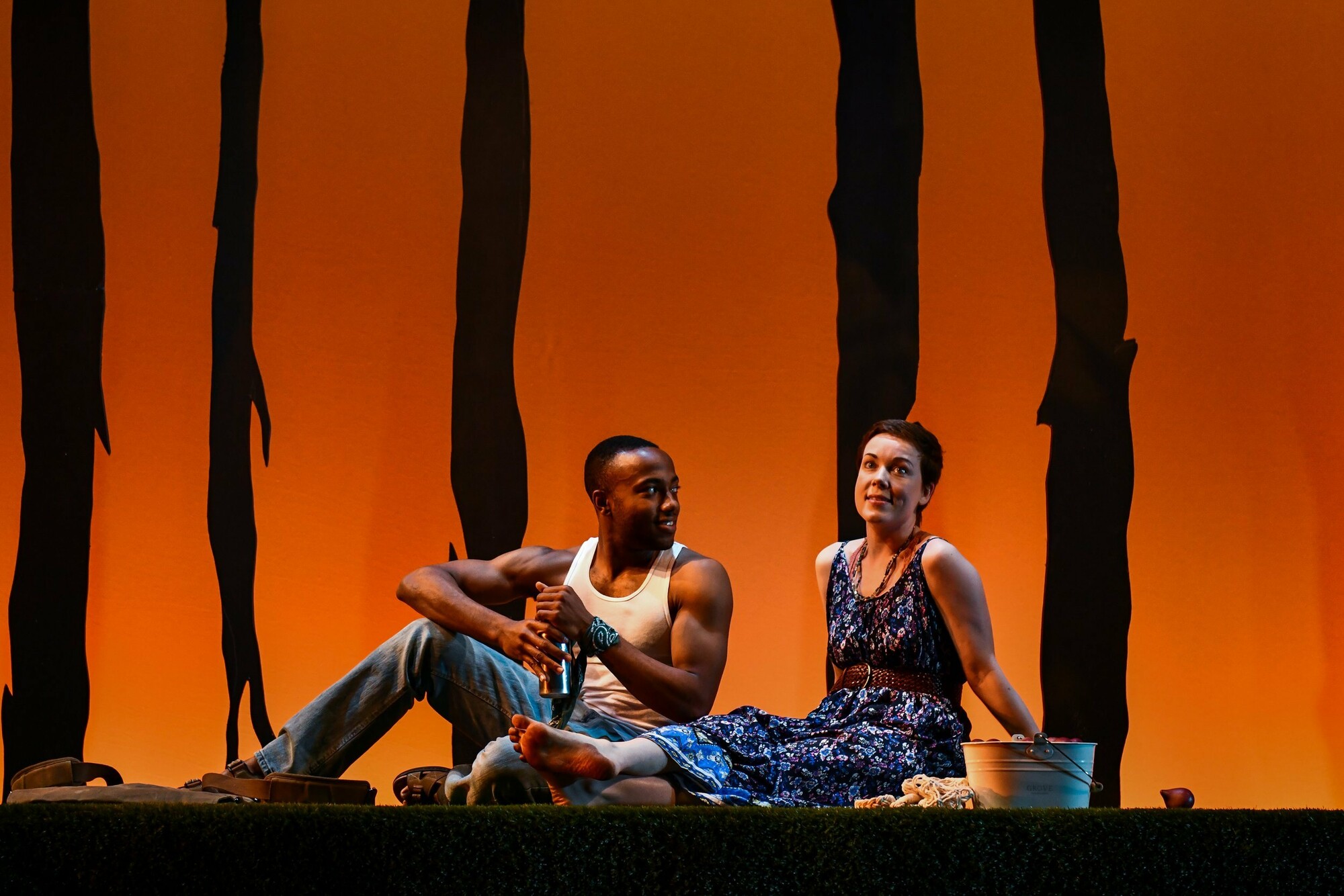 Two people sitting on a stage with an orange background behind them.