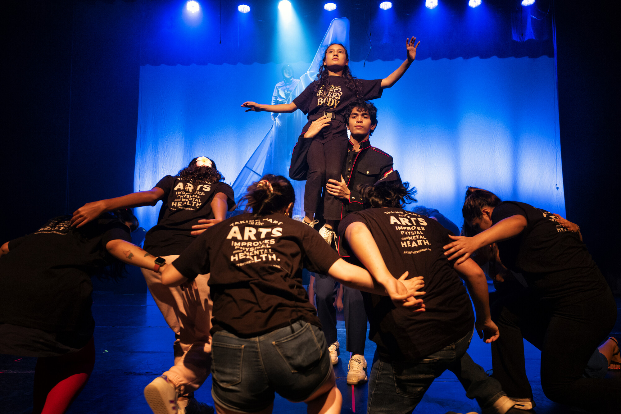 People on stage in black t-shirts creating a human tower with one person held up higher than the rest.