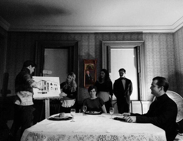 A black and white photo of people giving a presentation to people in a small room.