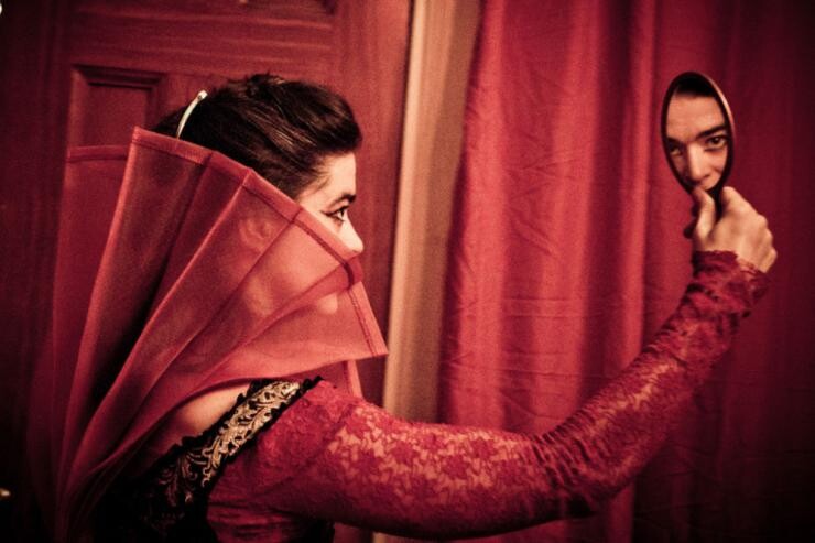 A woman in red looking at herself in a handheld mirror.