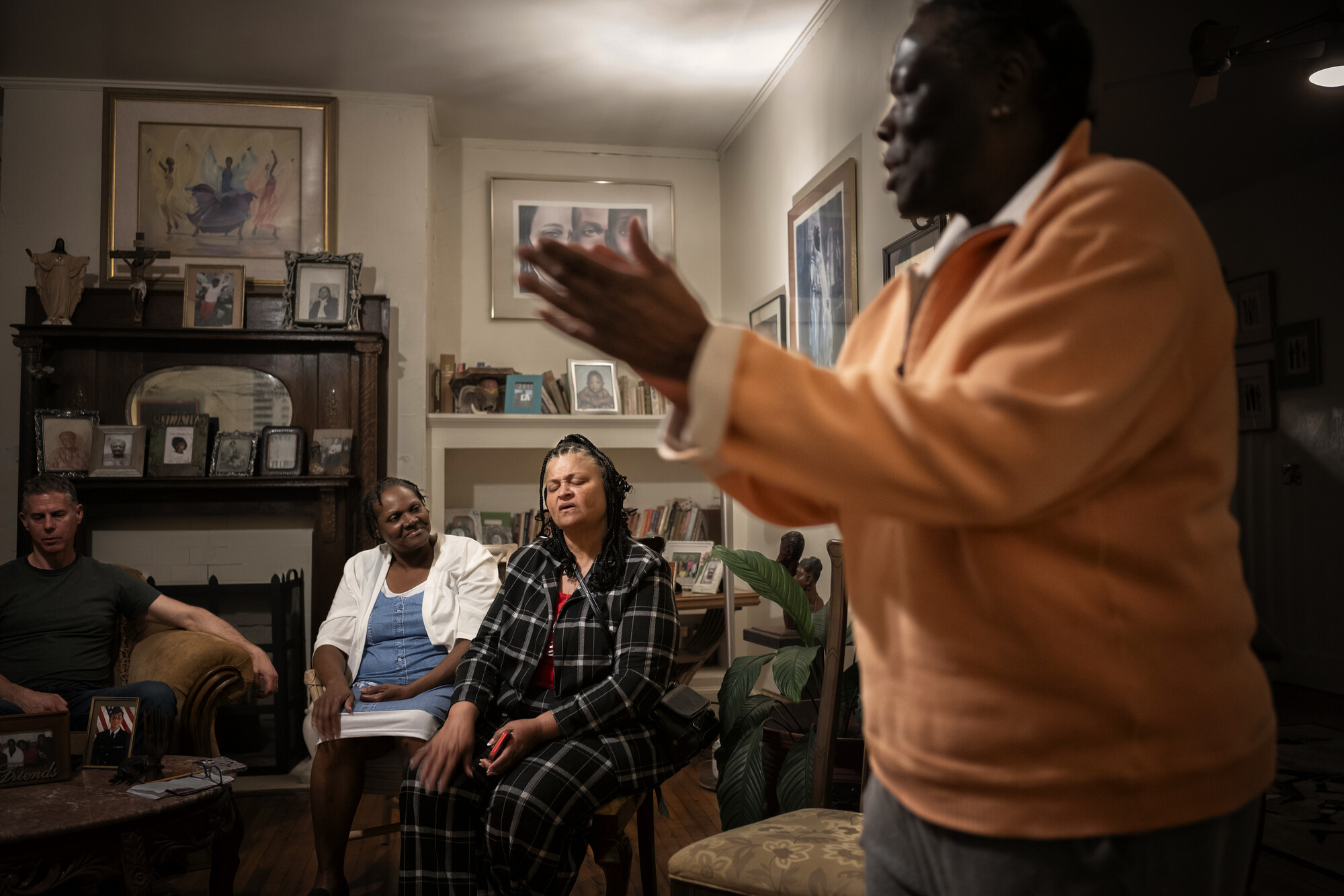 A man in a living room clapping while three seated people watch.