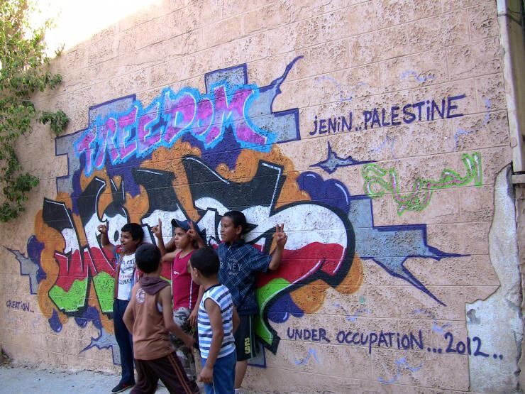 Children standing against a graffitied wall.