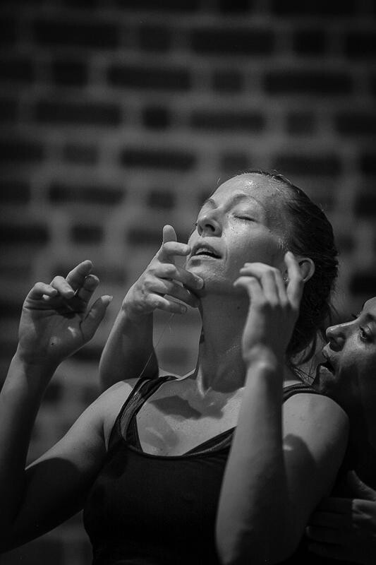 A black and white photo of a person looking slightly upwards with their hands raised and another person's hands behind them.