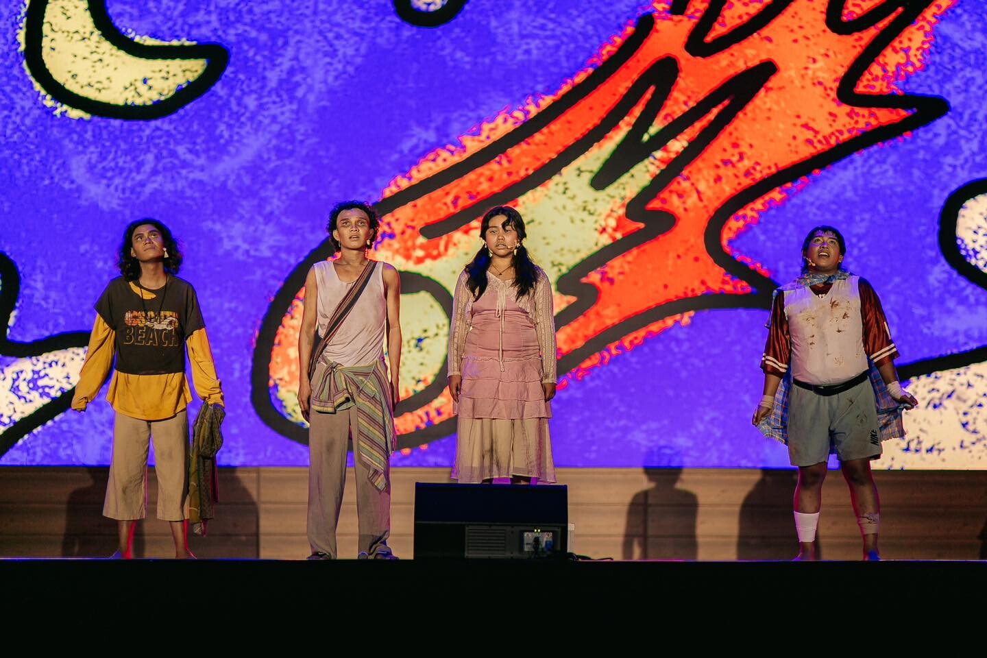A group of actors on stage with a colorful background.