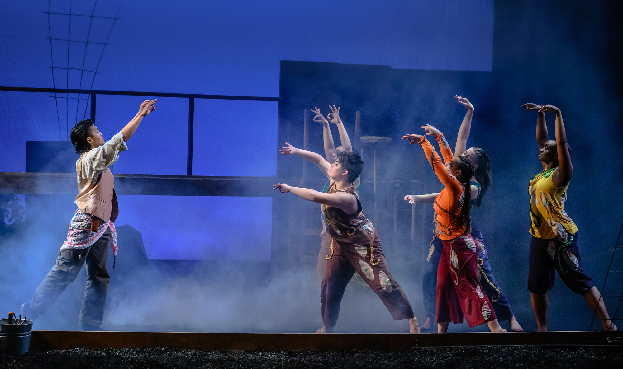 A group of dancers on stage in front of a dark blue background.