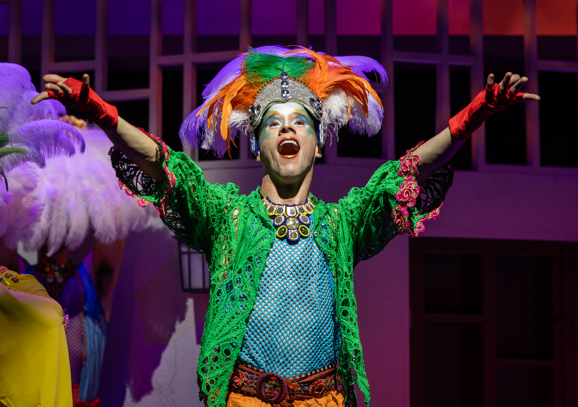 A person dressed in masquerade attire singing out dramatically.