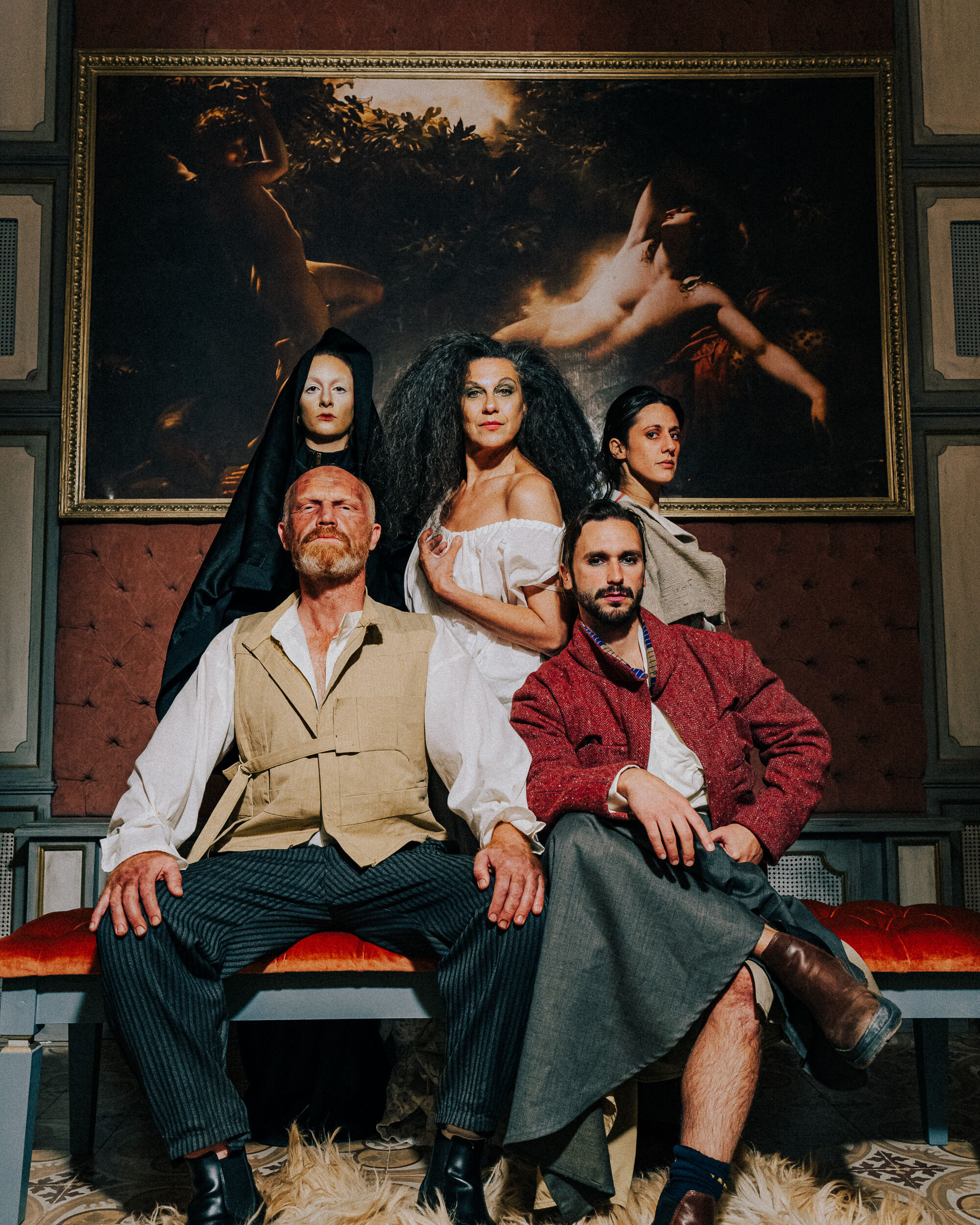 Five people dressed in reds, whites, and creams posing dramatically for a group photo.