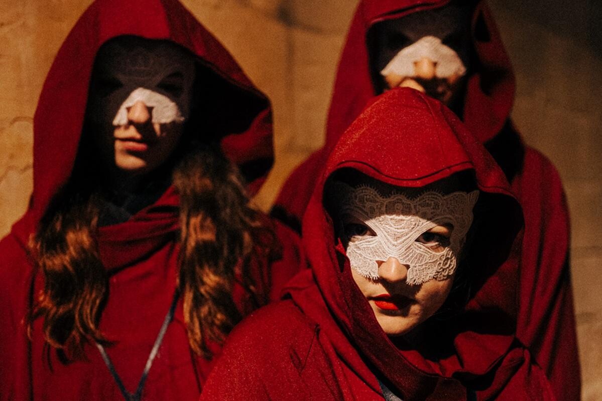Three people in white masks and red capes.