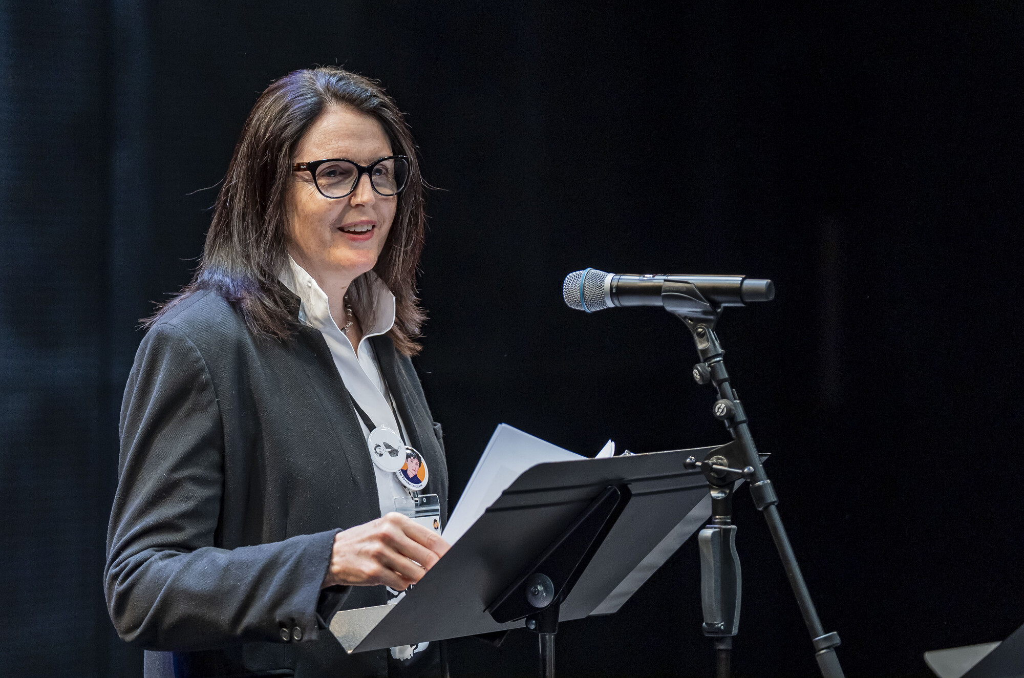 A woman in a black blazer giving a speech at a podium.