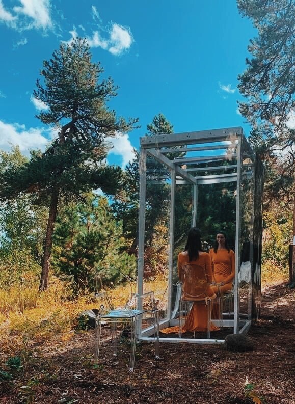 A person dressed in orange in a metal box in the wilderness.