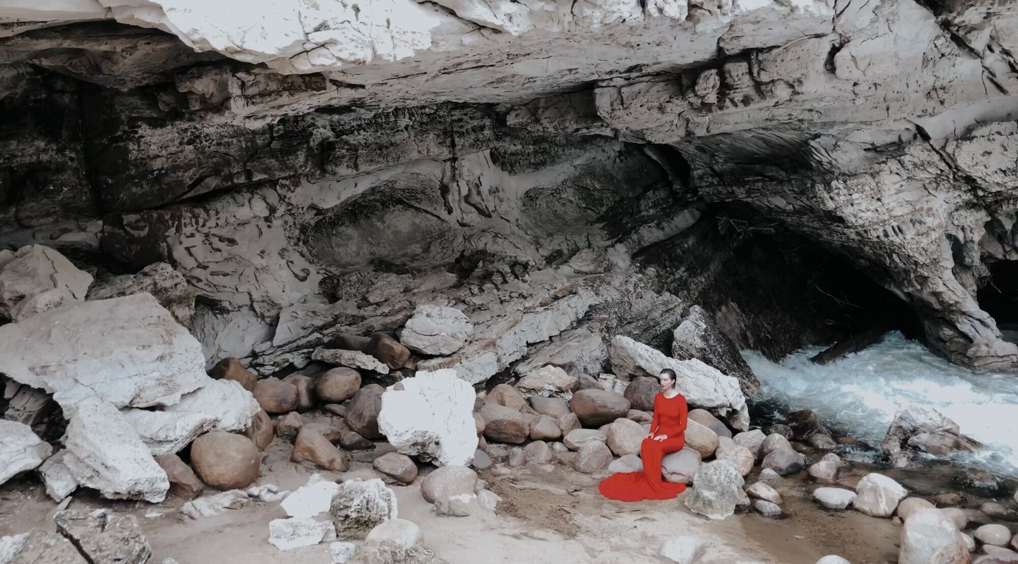 A woman in a long red dress in a rocky area.