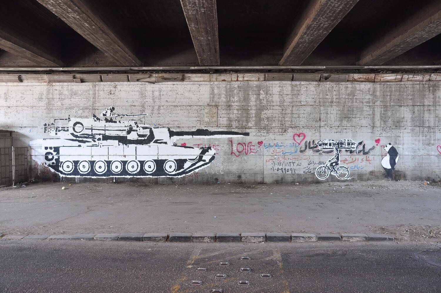 A wall painted with the image of a tank pointing its gun at a person on a bike.