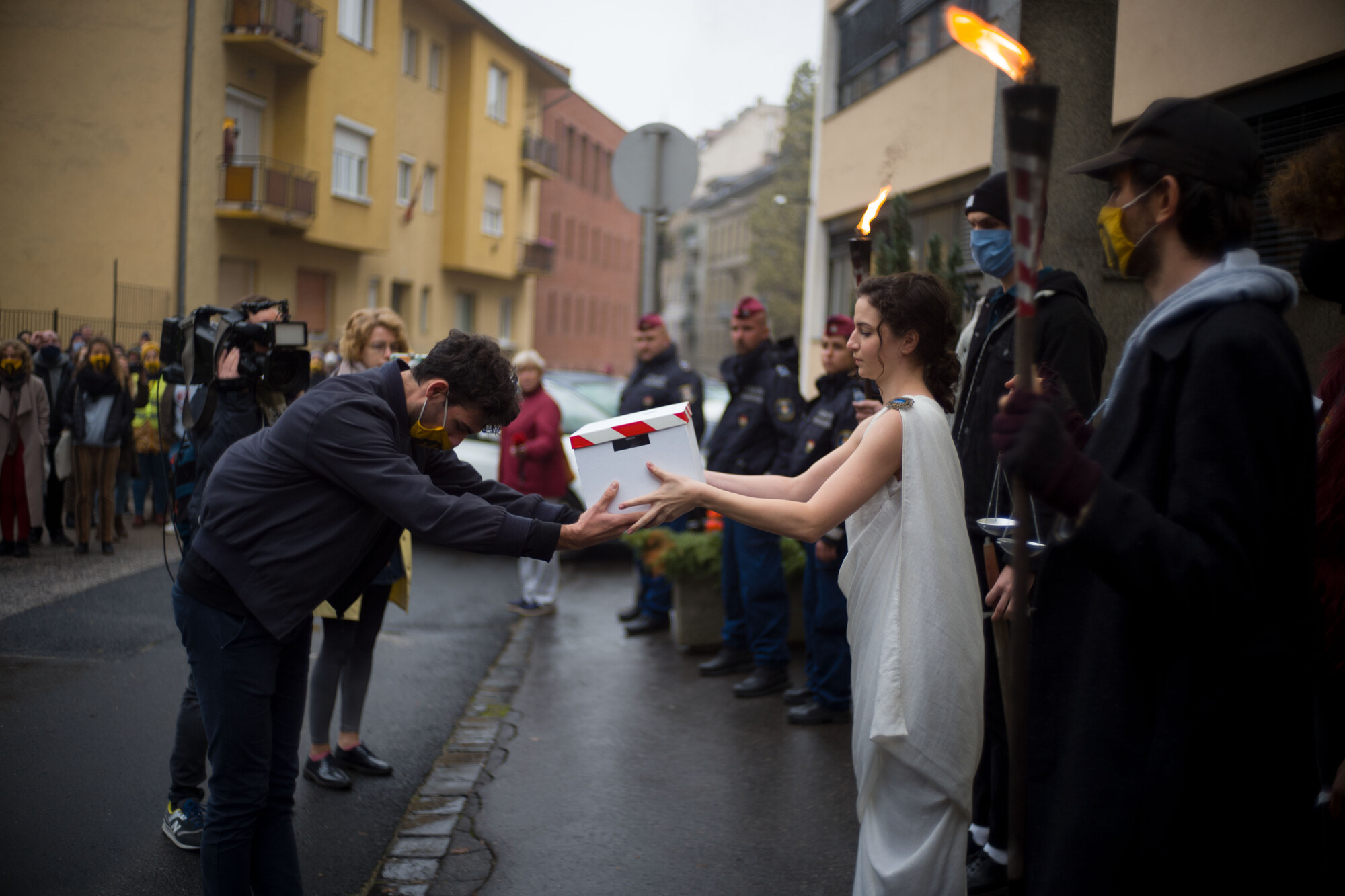 A person in a toga receiving a box from another person.