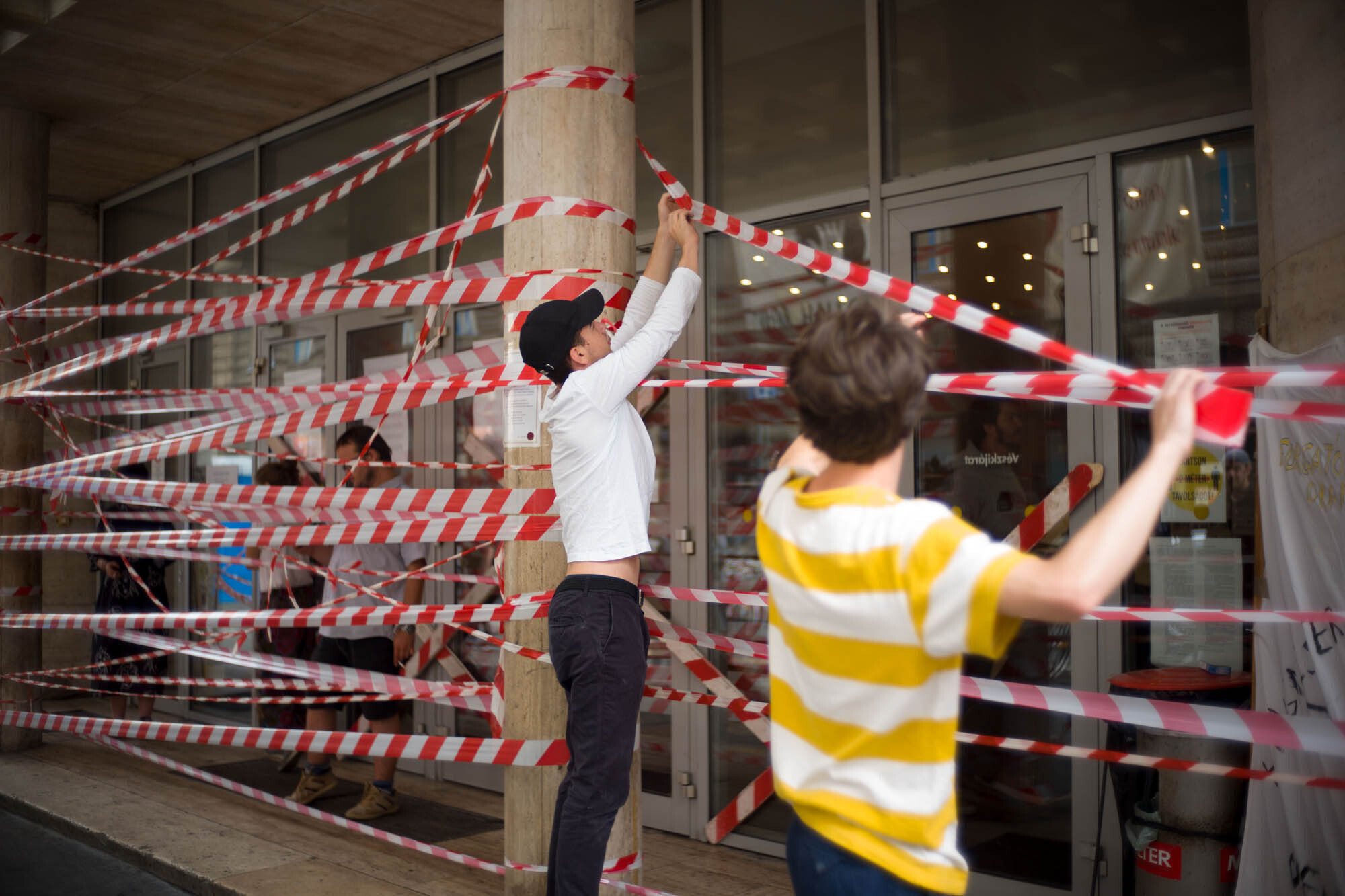 Two people putting up red and white striped tape.
