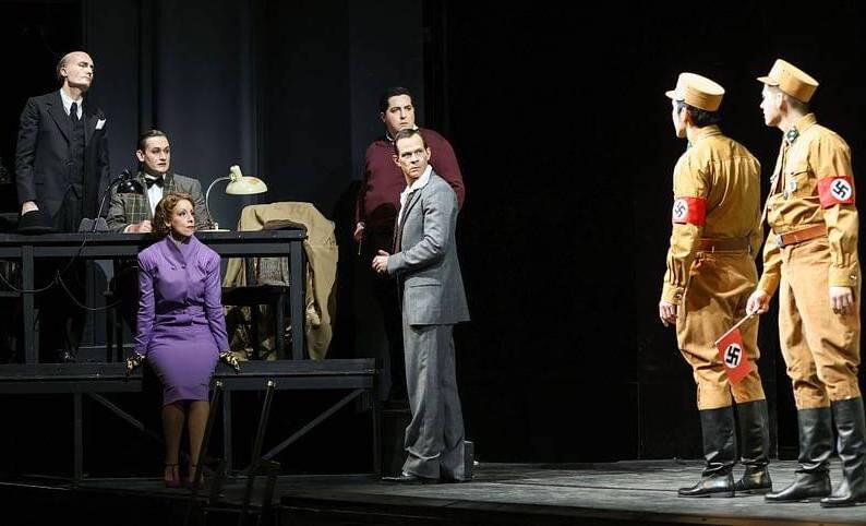 Actors on stage dressed in suits and Nazi costumes.