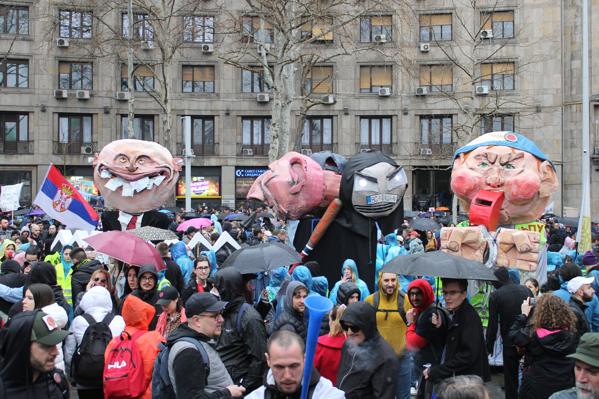A group of people outside at a festival with large puppets.