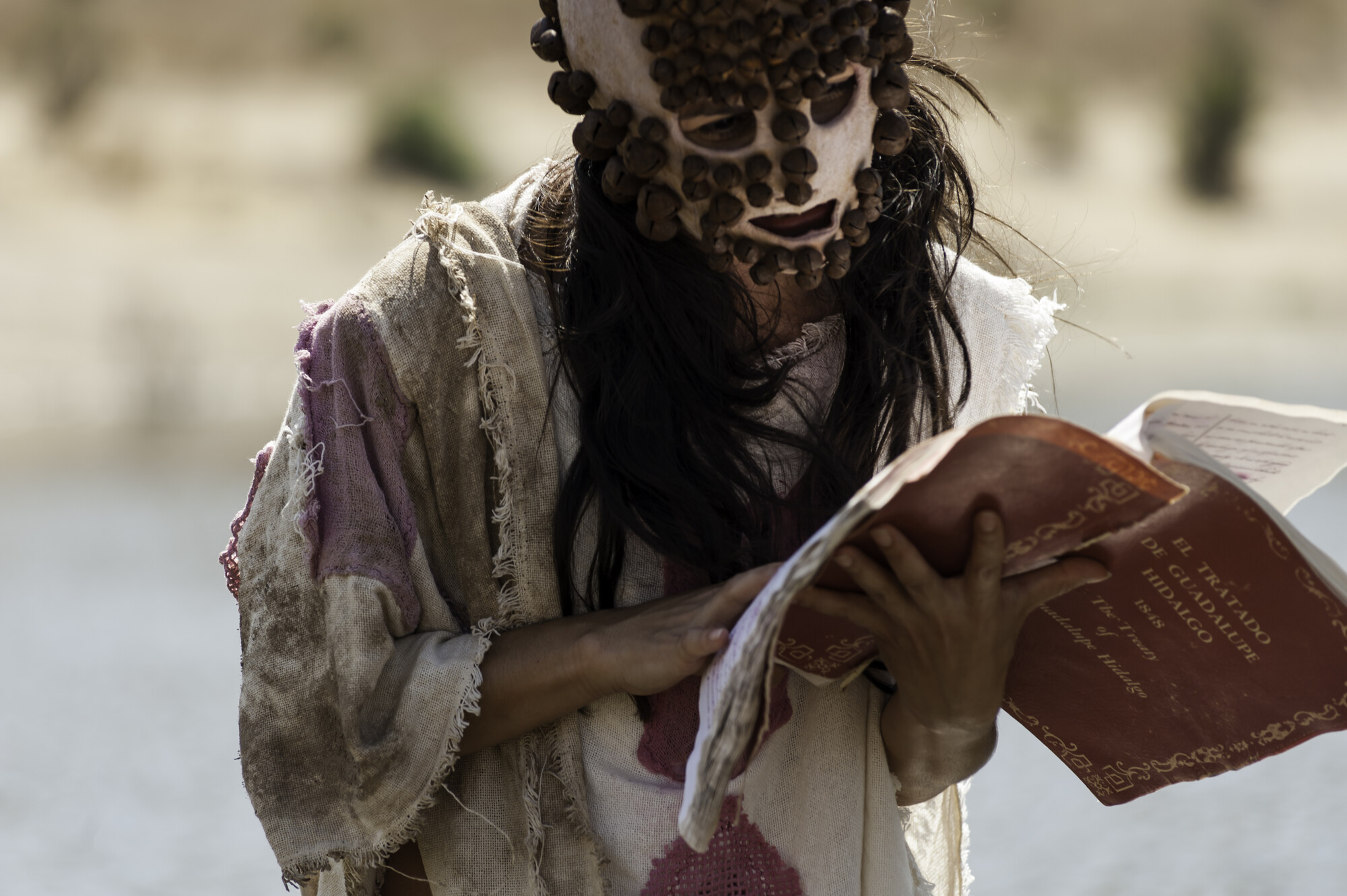 A person in a mask reading out of a book.