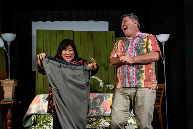 A woman holding up a pair of pants and a man laughing.