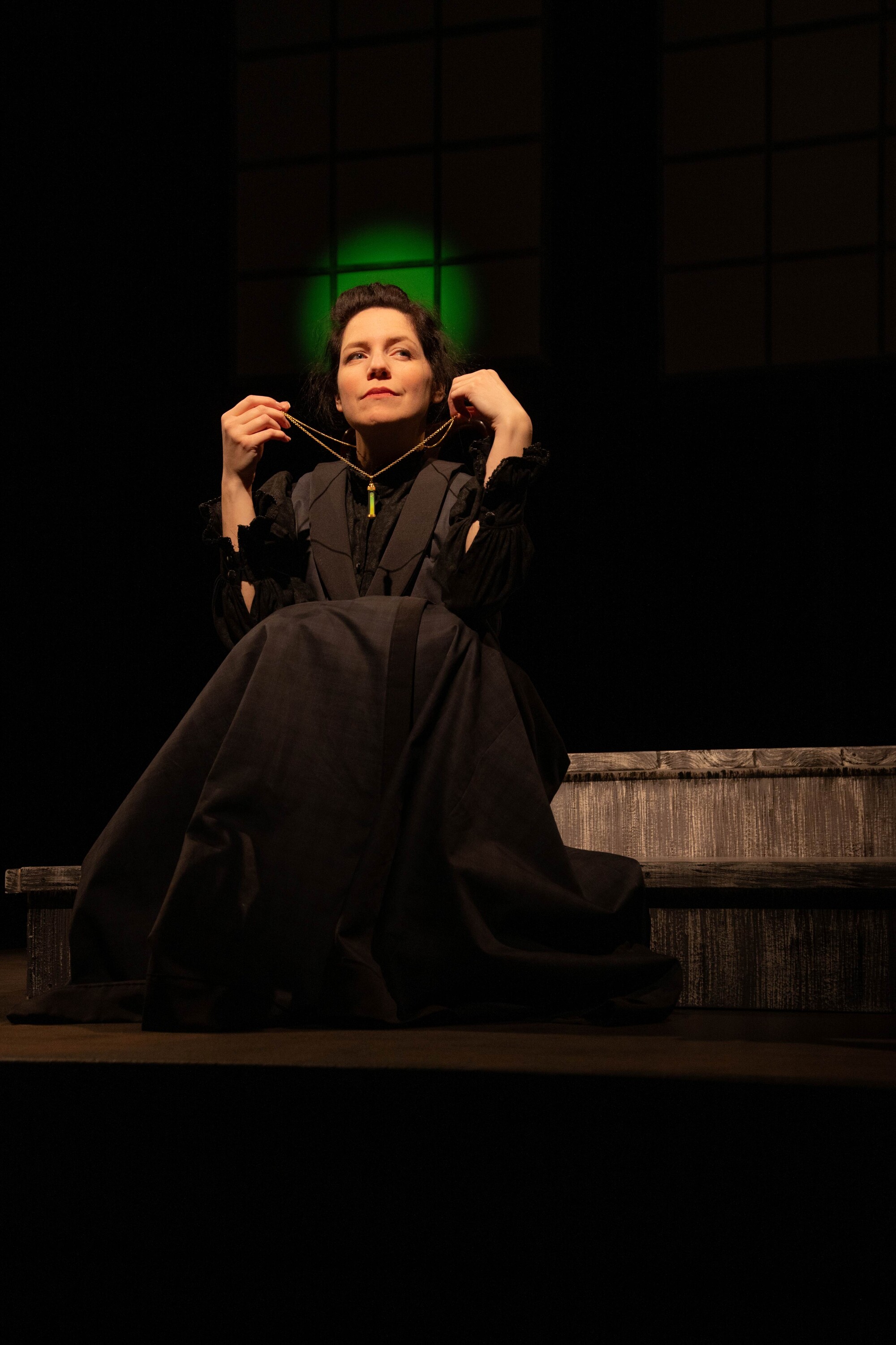 A woman in a black victorian style down holding a necklace up.