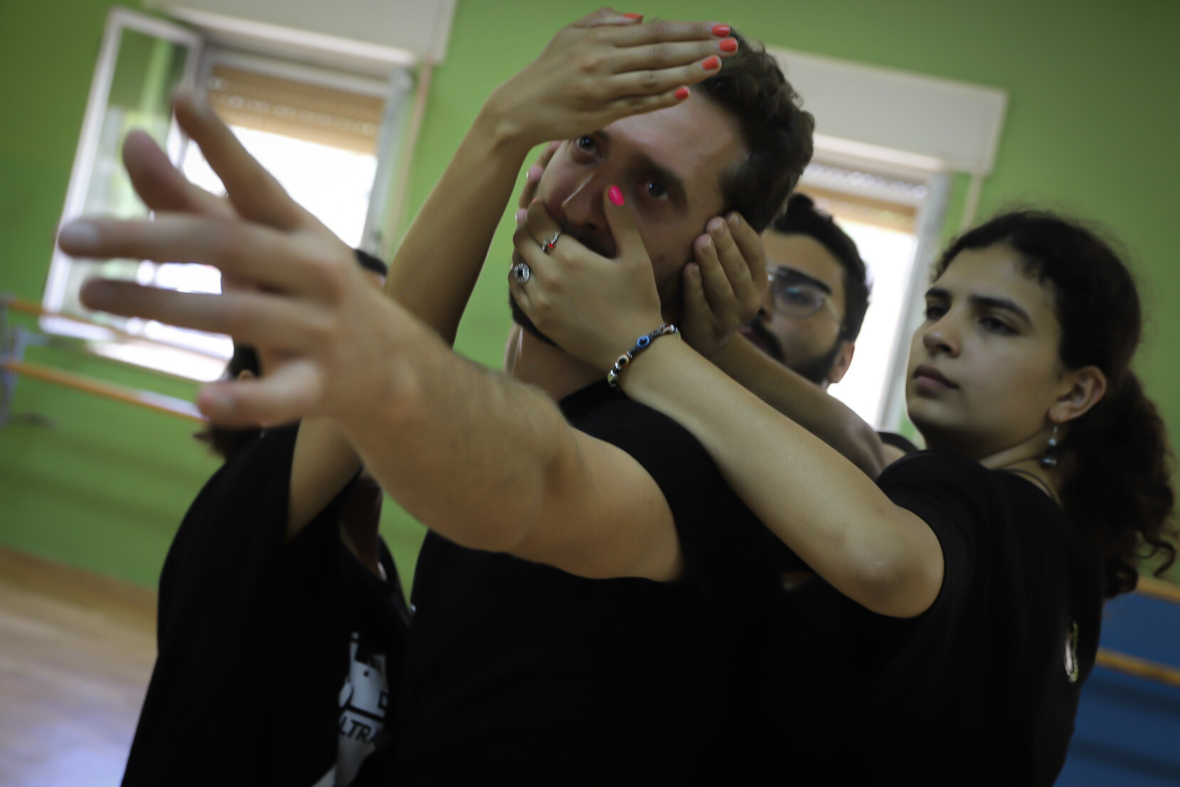 A man reaching forward while people grab on his mouth and head from behind.