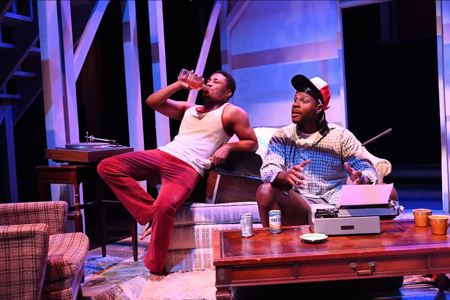 Two people sitting in a living room set on stage.