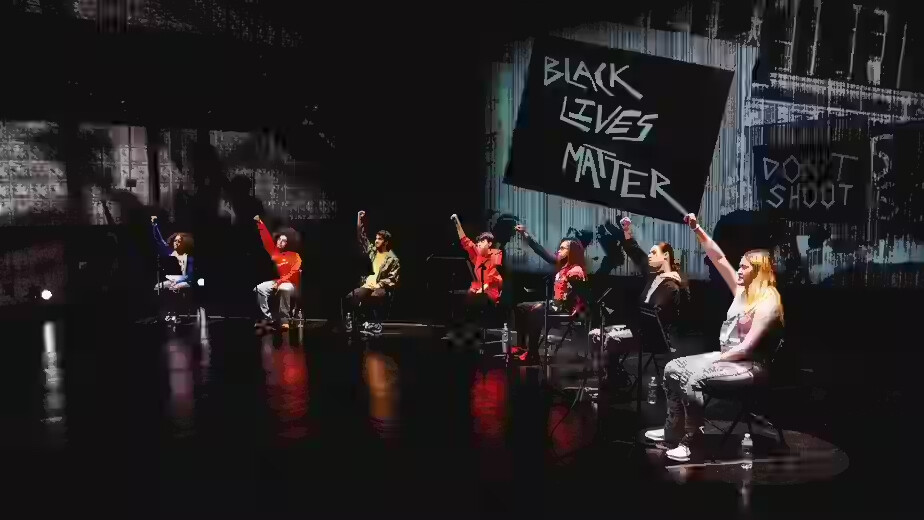 A row of people sitting on stage raising their hands.