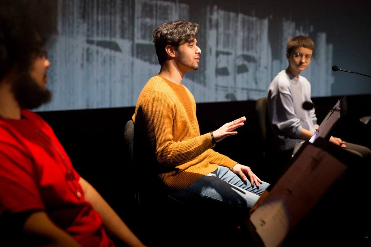A few people sitting on chairs on stage having a conversation.