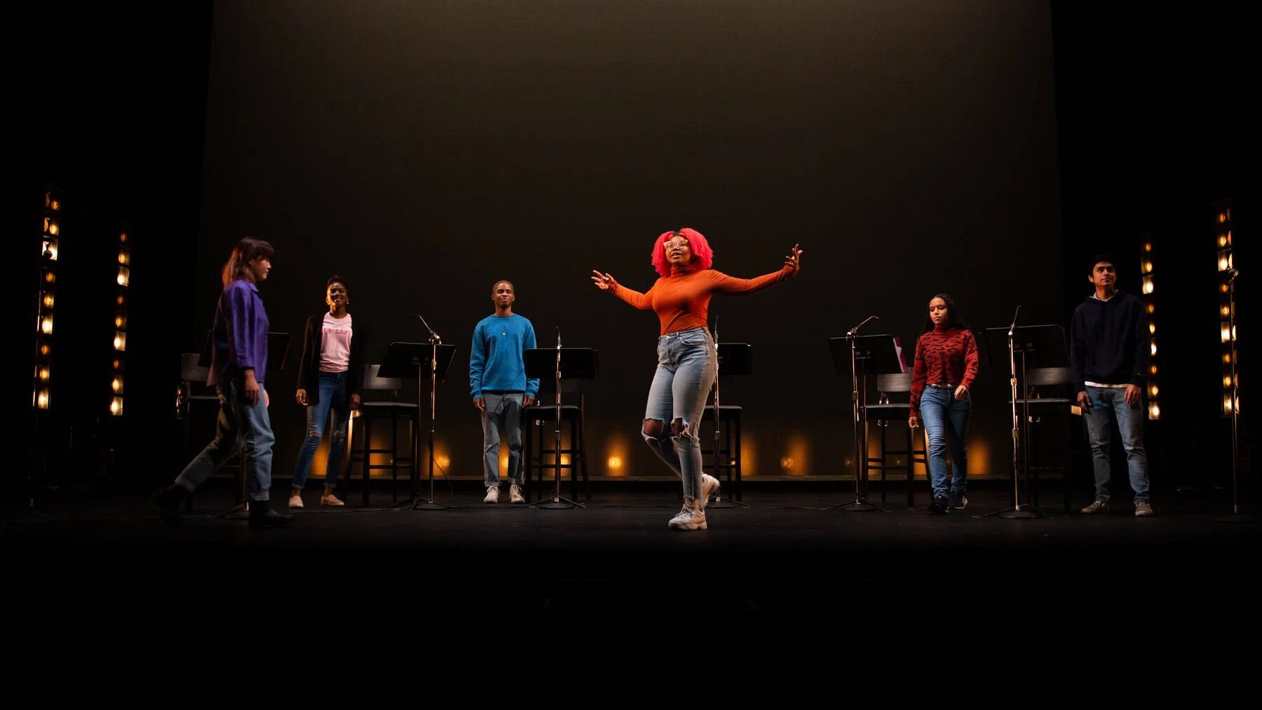 A group of actors on stage jumping around. 
