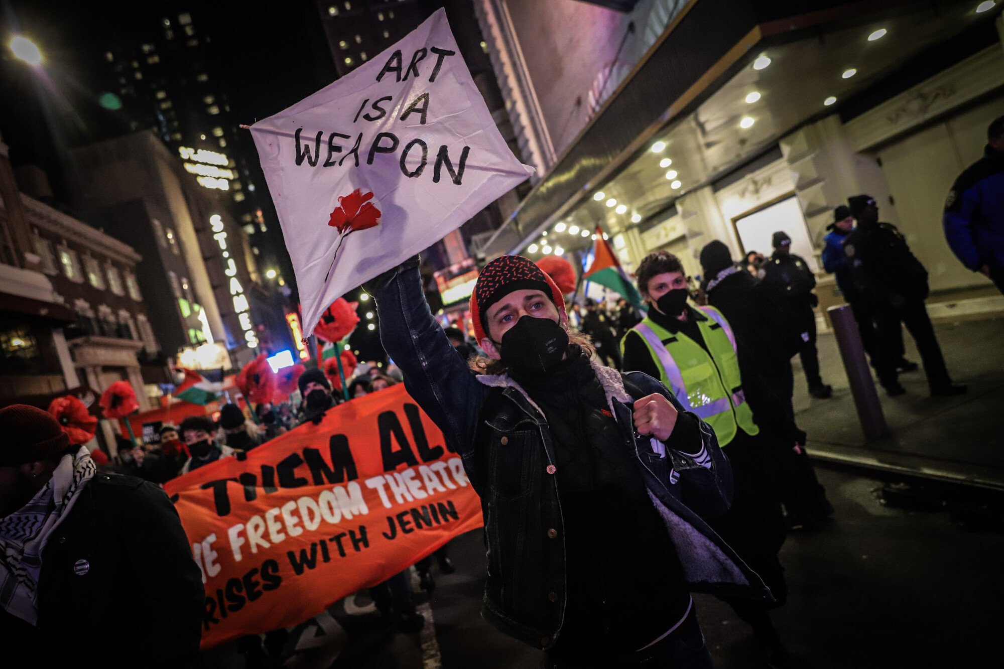 A person at a protest holding a sign reading Art Is A Weapon.