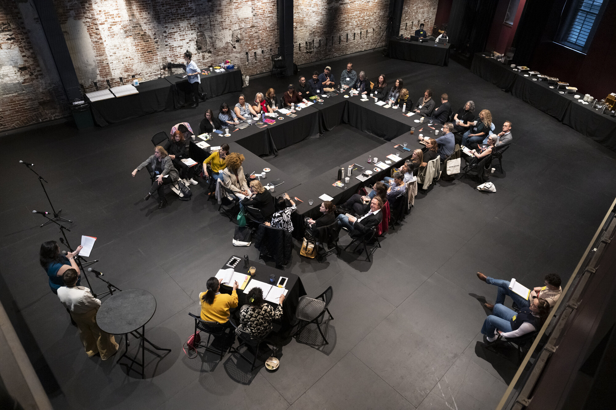 A group of people sitting around a table in a black box theatre.