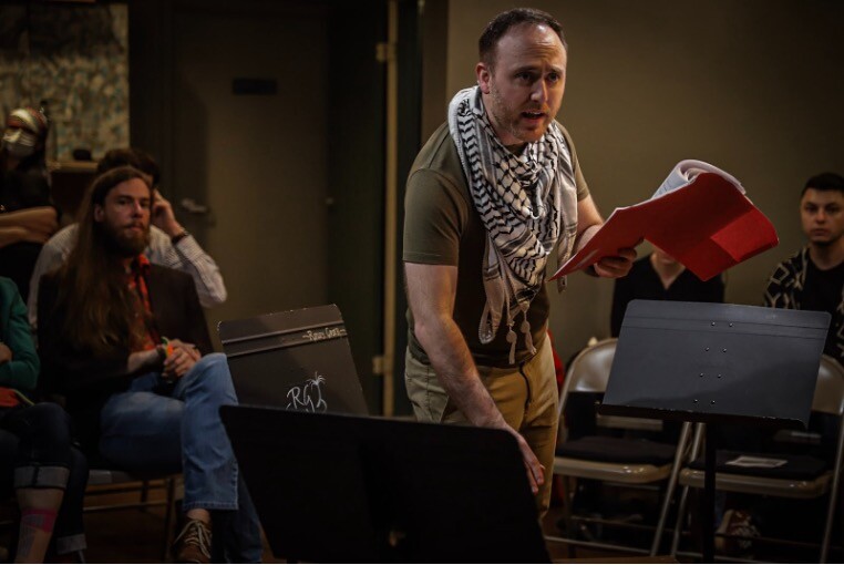 A man in a keffiyeh reads from a script.