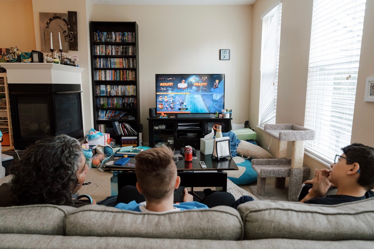 Three people sit on a couch watching a tv screen.