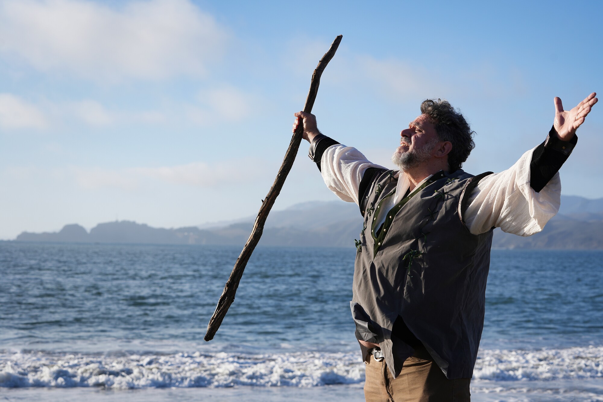A man stands with his arms outstretched before a body of water.