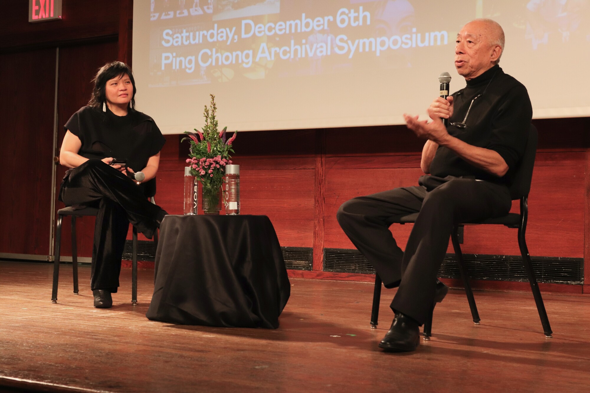 Two people talk onstage at a symposium.