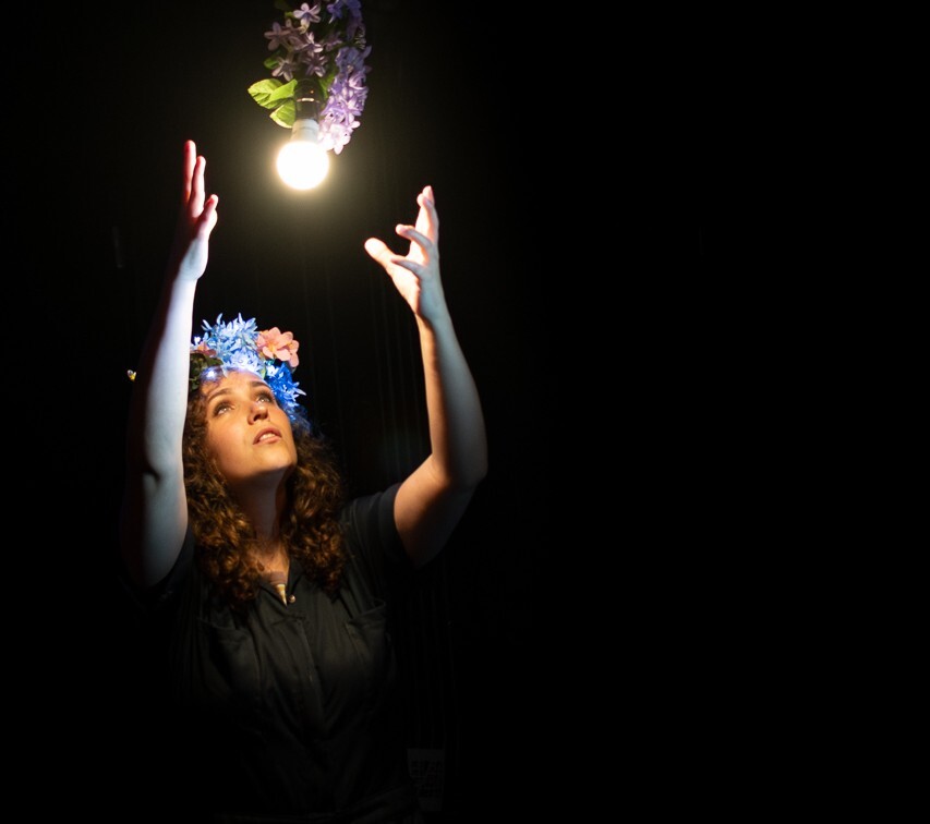 An actor looks up at a lightbulb covered with flowers.