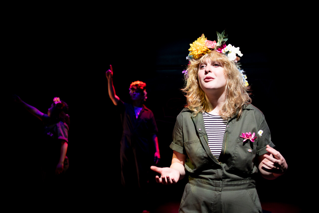 An actor with flowers on her head speaks to the audience.
