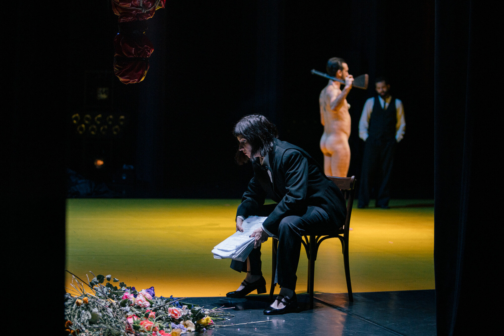 A person sits in a chair onstage with a naked man behind her.