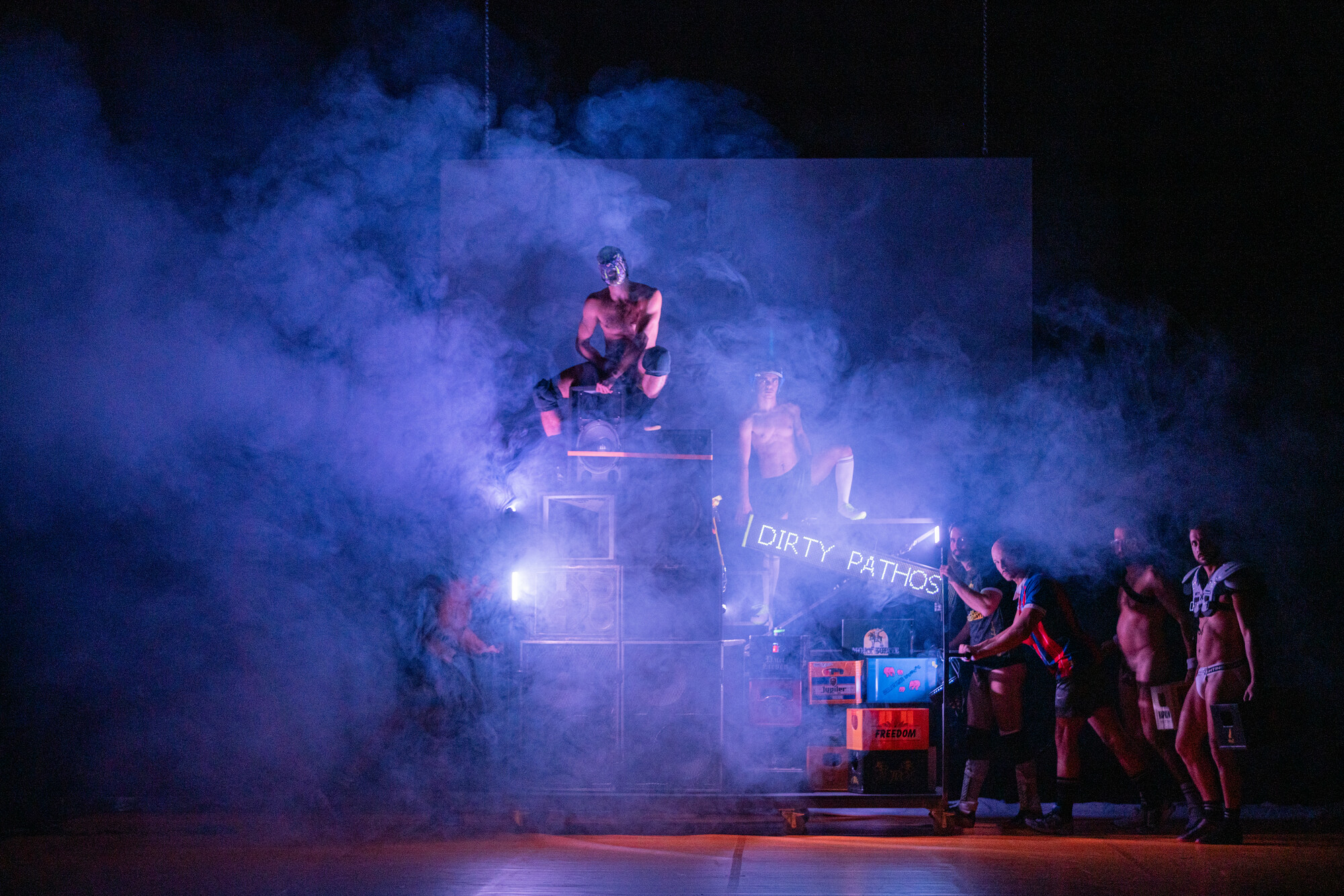 A group of people stand naked or partially clothed onstage.